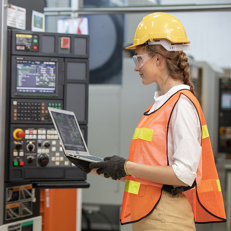 Factory worker is programming a CNC milling machine with a tablet computer. engineering and worker woman in safety hard hat and reflective cloth using lathe machine inside the factory.